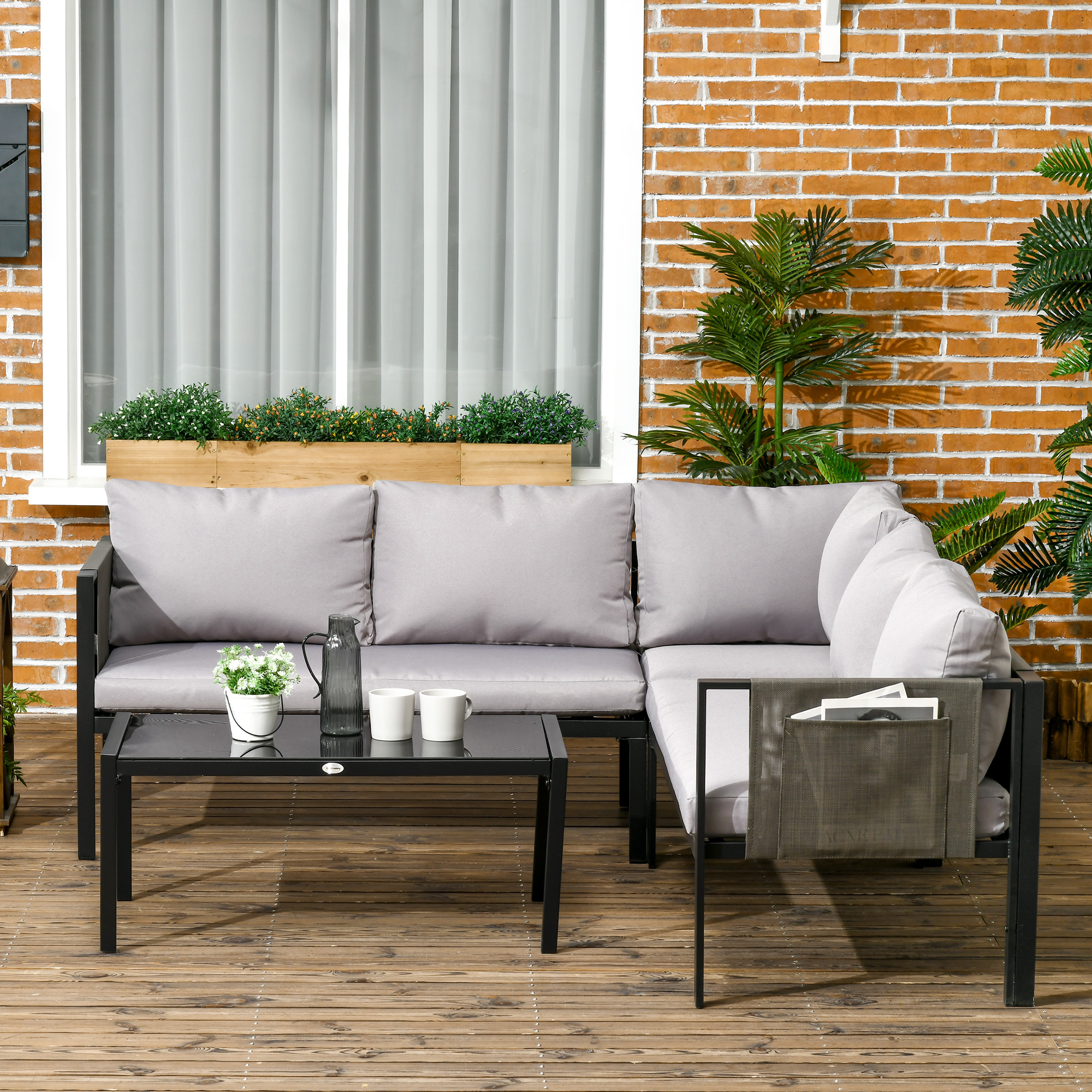 Divano componibile grigio con tavolino nero, brocca, tazze e piante su deck legno.