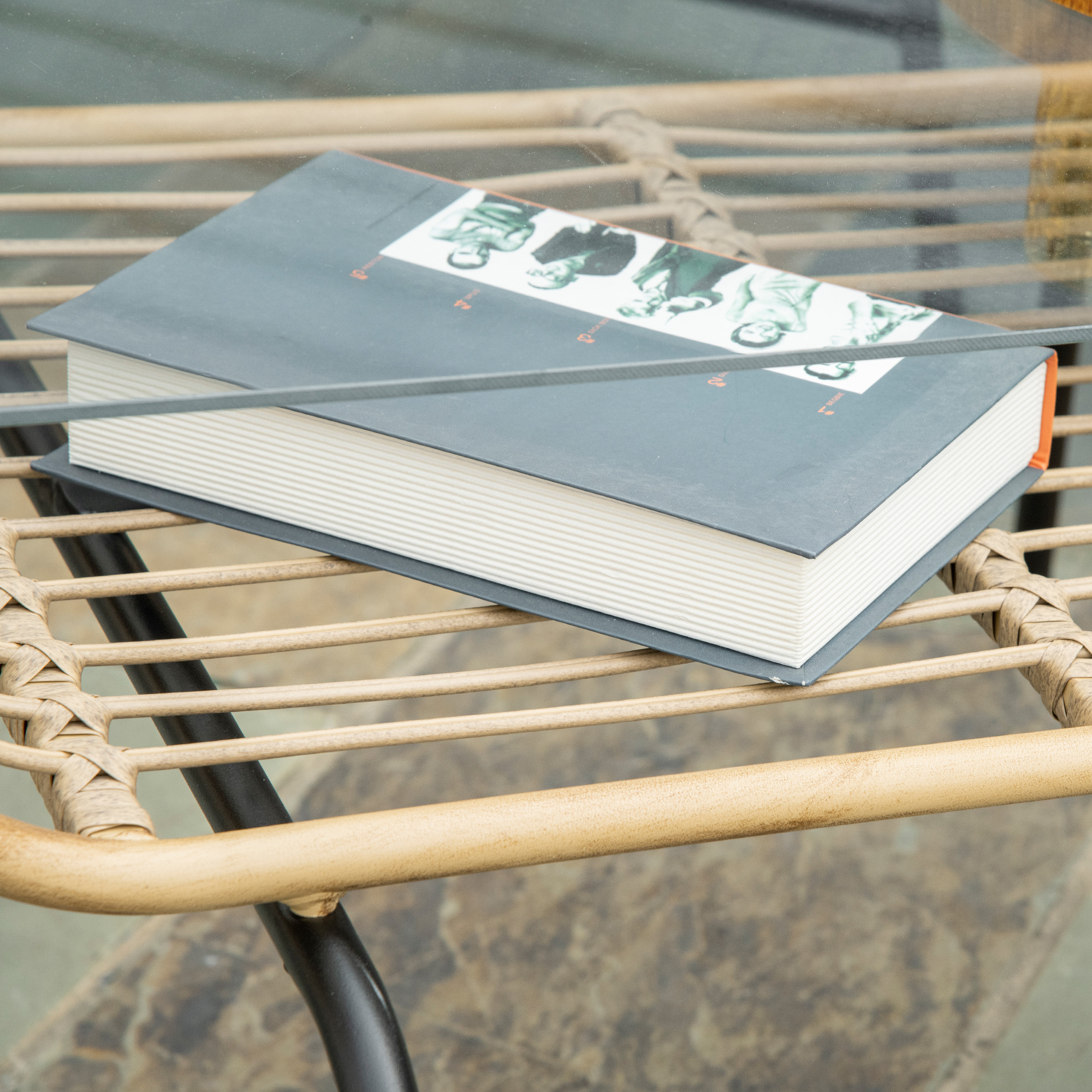 Un libro aperto con copertina nera e dorso arancione giace su un tavolo di rattan.