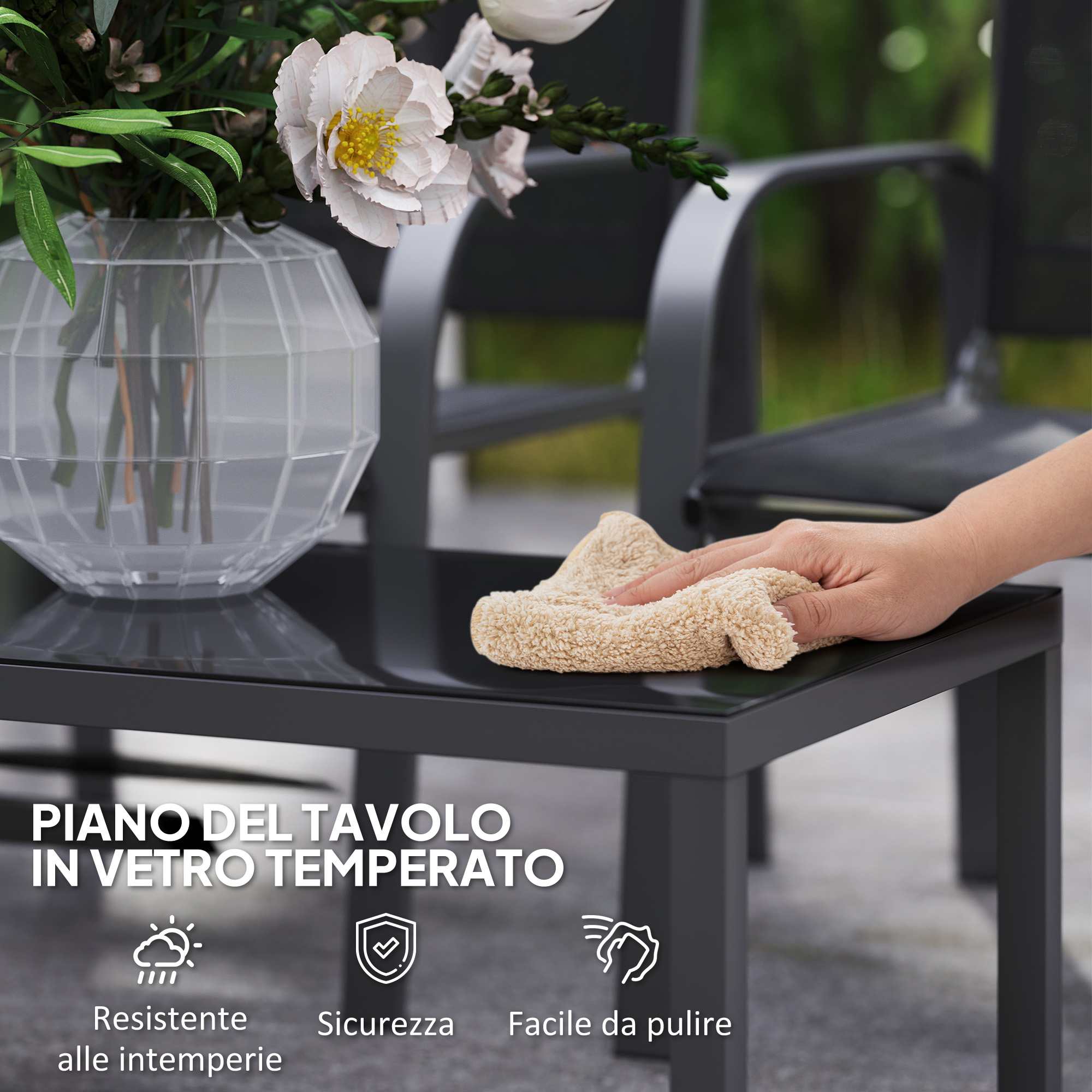 Una mano pulisce un tavolo nero con un panno beige. Fiori in vaso.