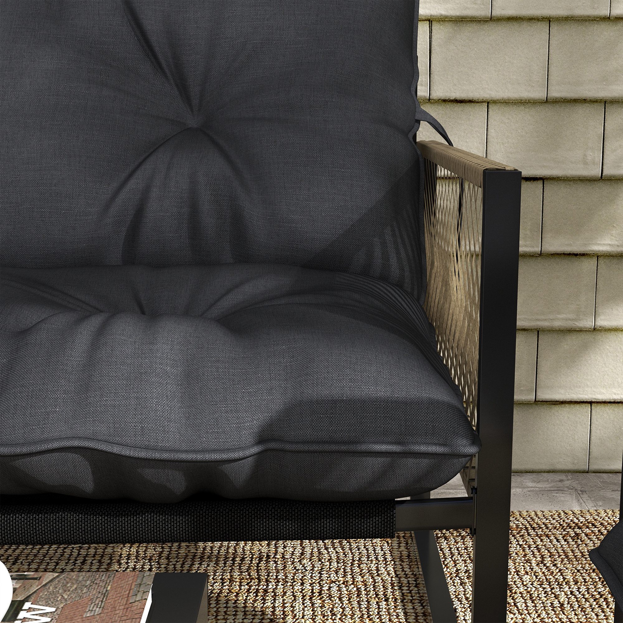 Divano da esterno grigio scuro con cuscini davanti a un muro piastrellato chiaro.