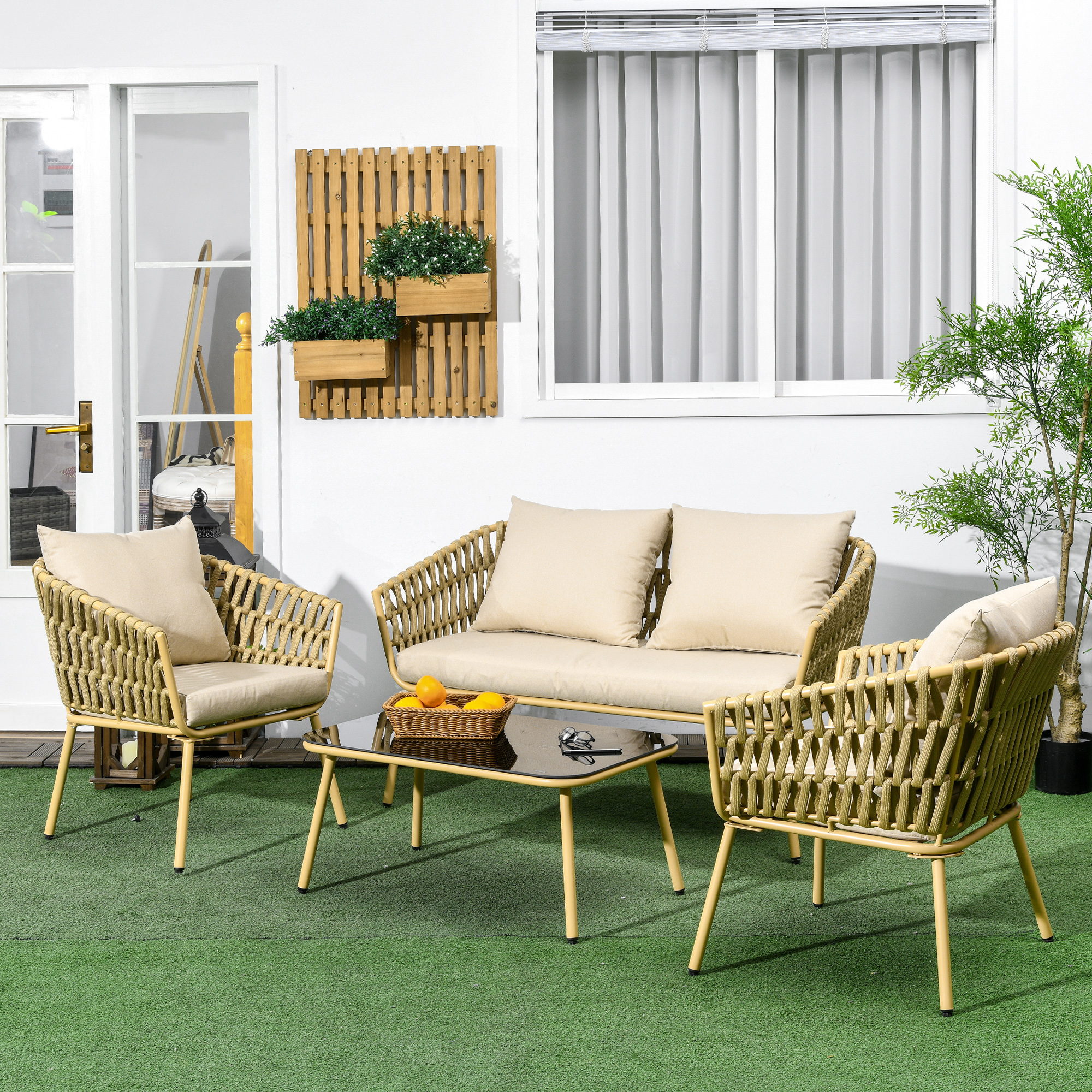 Divano e due poltrone beige intrecciati su erba sintetica davanti a una finestra.