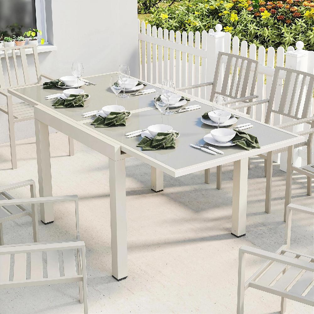 Un tavolo allungabile con sedie bianche e apparecchiatura per la tavola su un patio con giardino.