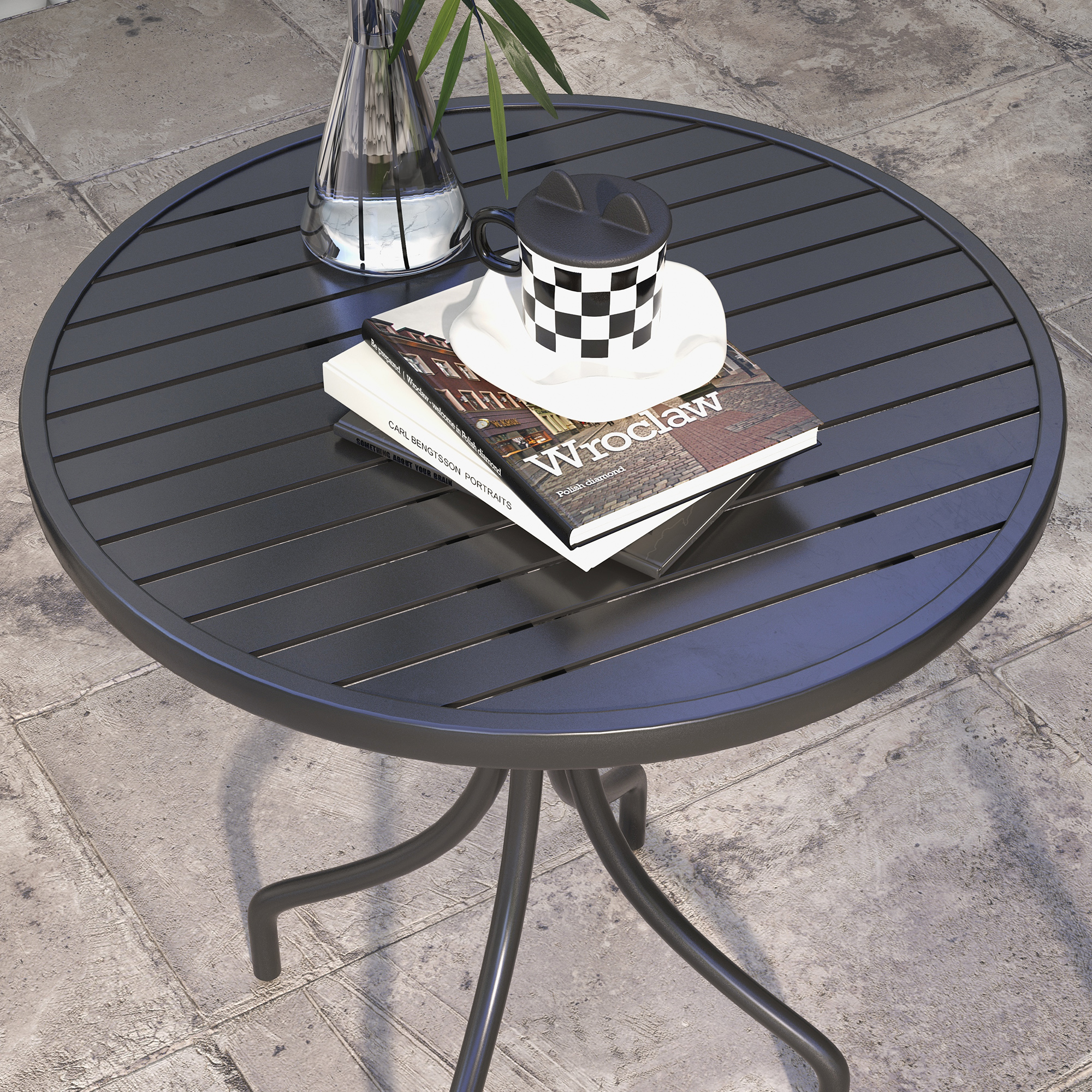 Un tavolo rotondo nero con vaso di vetro, tazza e libri su un patio di pietra.