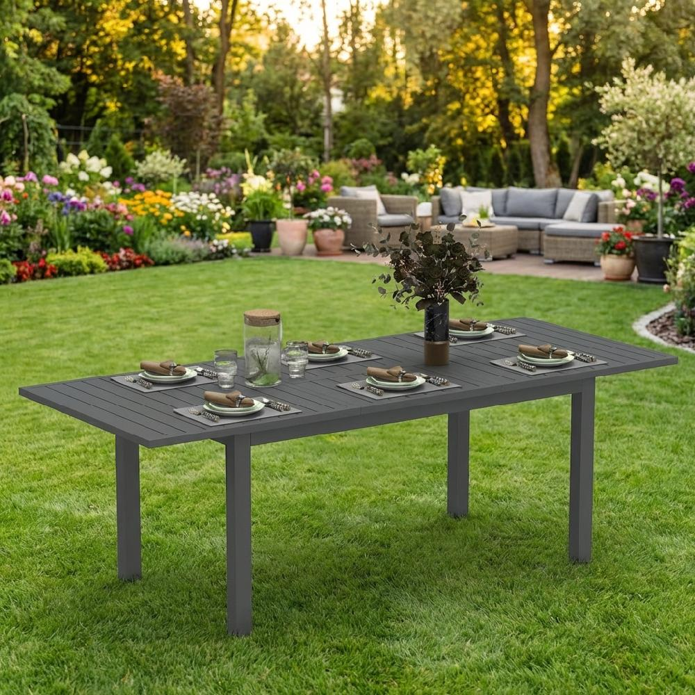 Un tavolo da giardino grigio apparecchiato su un prato verde, con fiori e sedute.