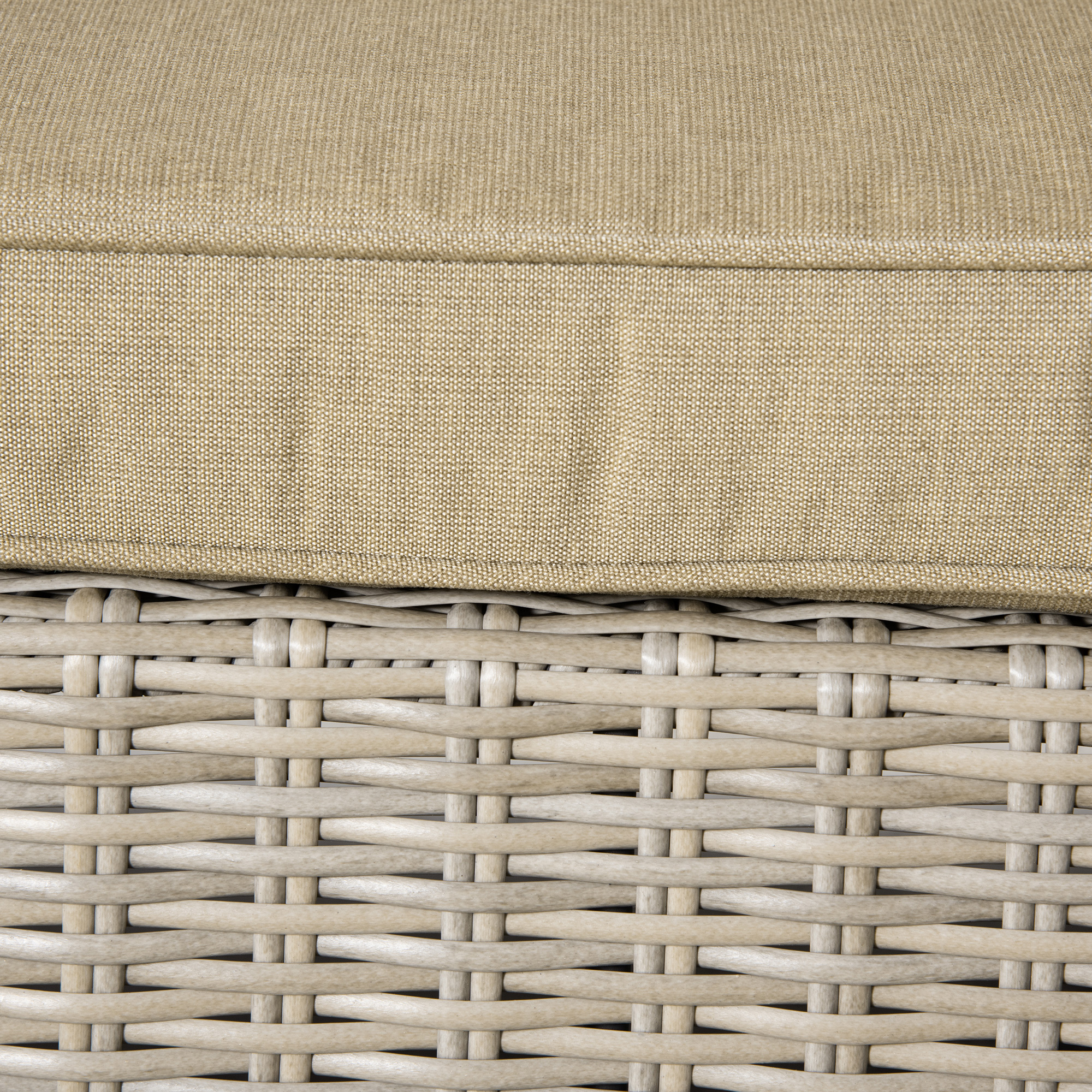 Cuscino in tessuto beige su trama di rattan grigio chiaro.