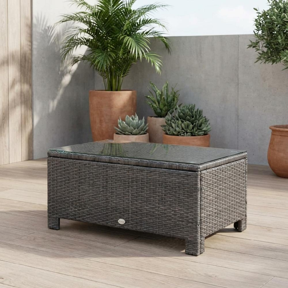 Tavolino da caffè in rattan grigio con piano in vetro su terrazza in legno, piante dietro.