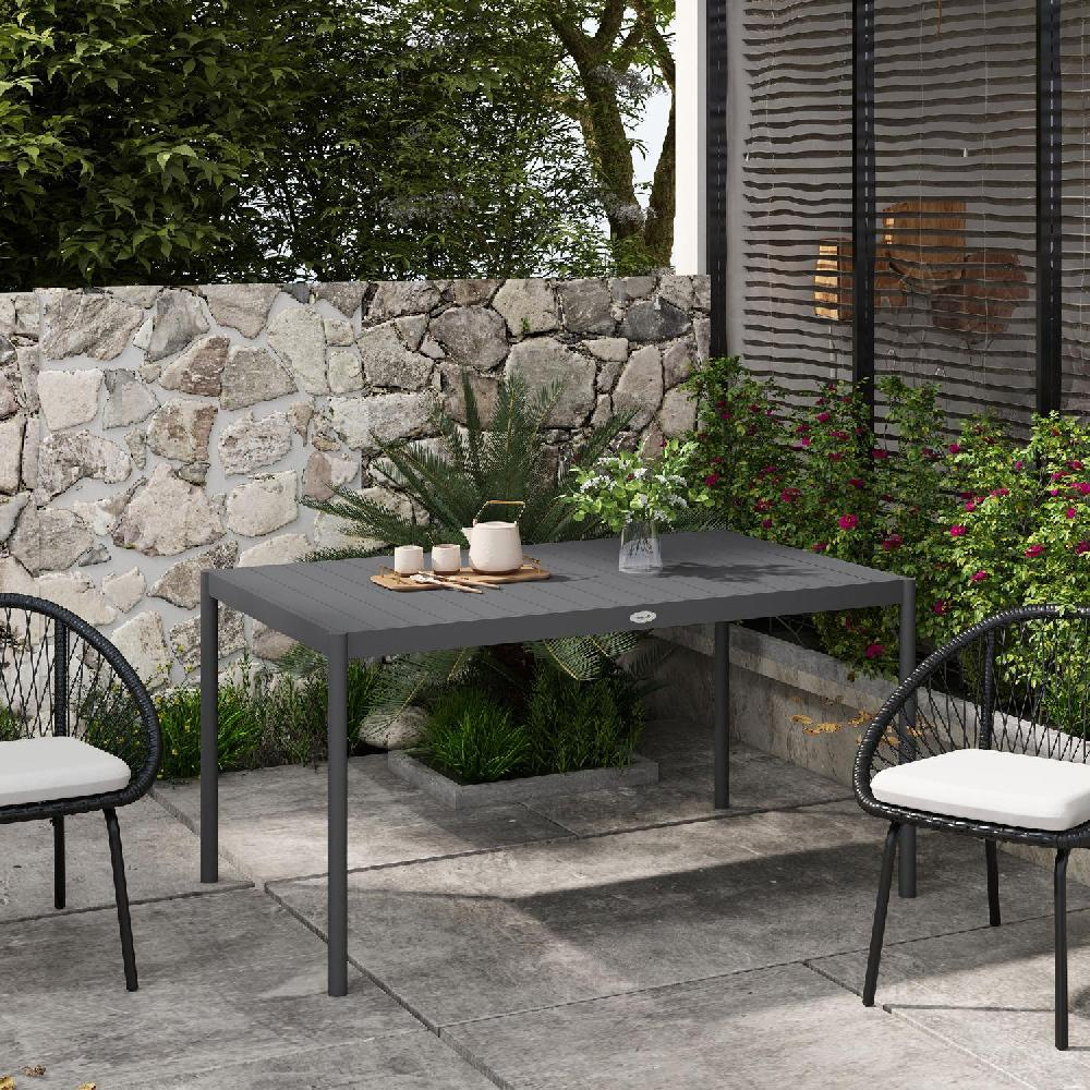 Un tavolo scuro con due sedie su un patio, muro di pietra e piante.