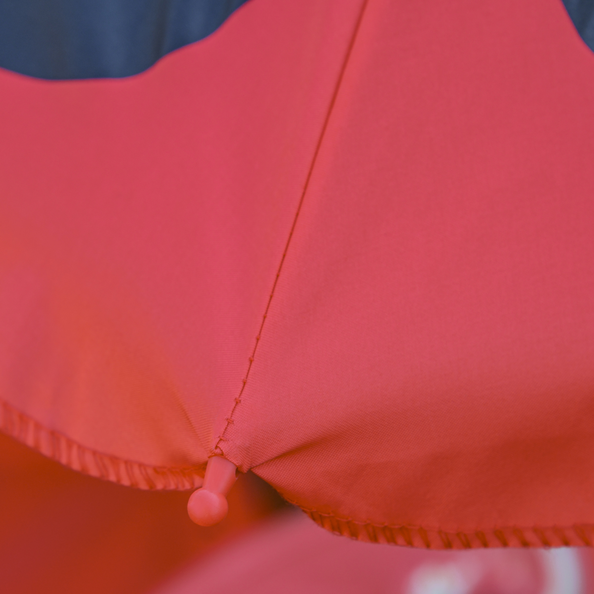 Primo piano di tessuto rosso con cucitura e un piccolo bottone rosa.