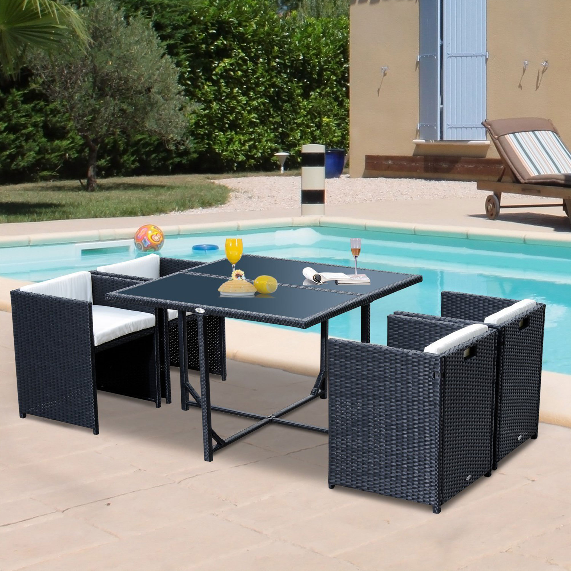 Un set da pranzo in rattan nero con quattro sedie si trova vicino a una piscina. Bicchiere e palla sul tavolo.