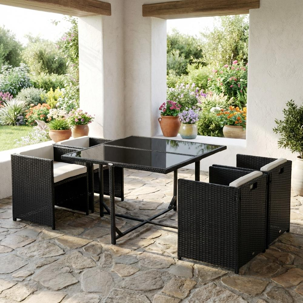 Set da pranzo in rattan nero con tavolo in vetro e quattro sedie su patio in pietra.