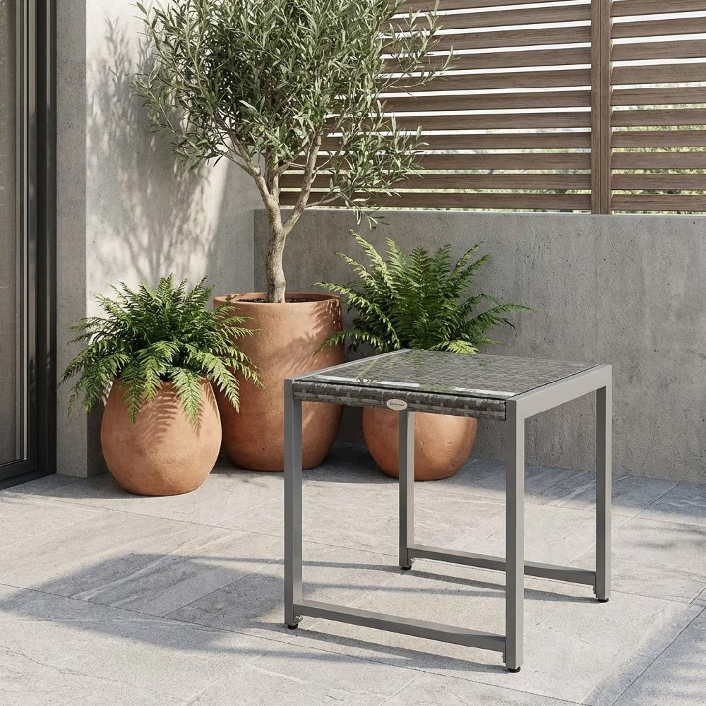 Un tavolino con piano in vetro si trova su un patio in pietra accanto a grandi piante in vasi di terracotta.