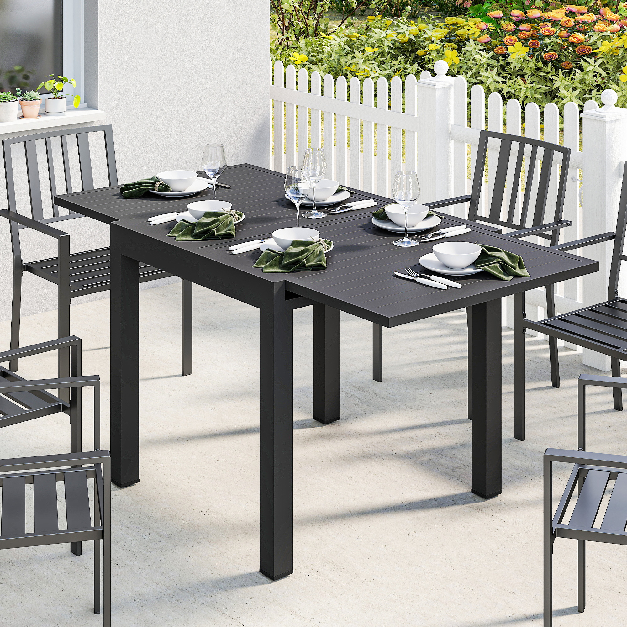 Set da pranzo in metallo grigio scuro su patio con recinzione bianca e fiori.