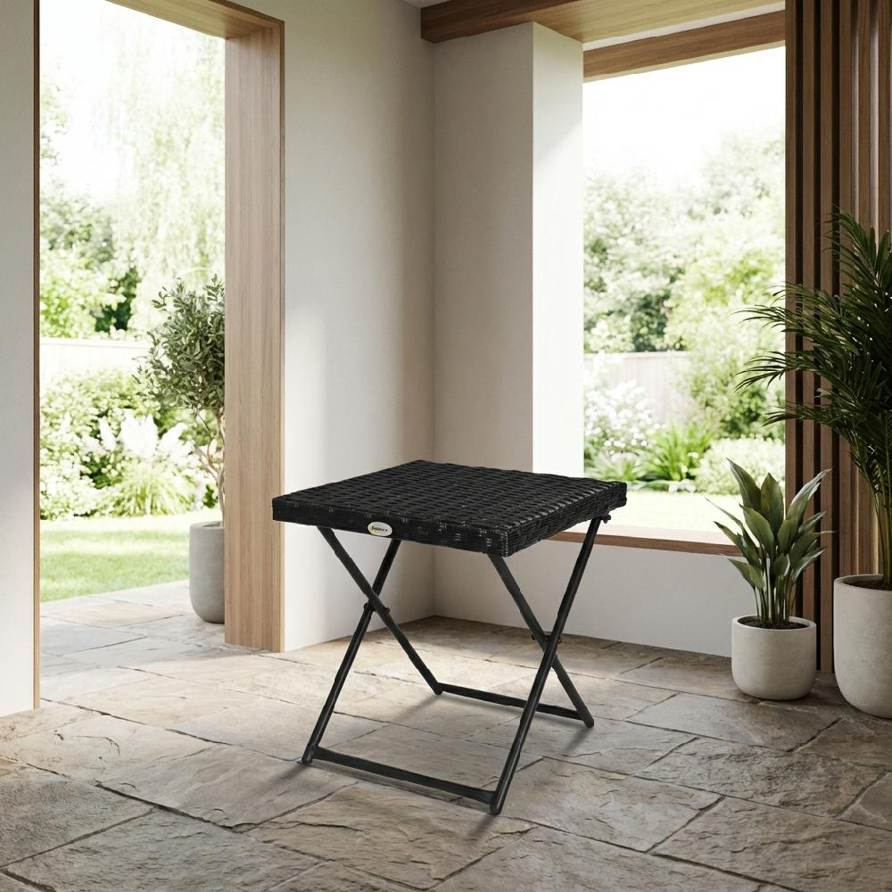 Un tavolo pieghevole nero in rattan si trova su un patio di pietra con piante.
