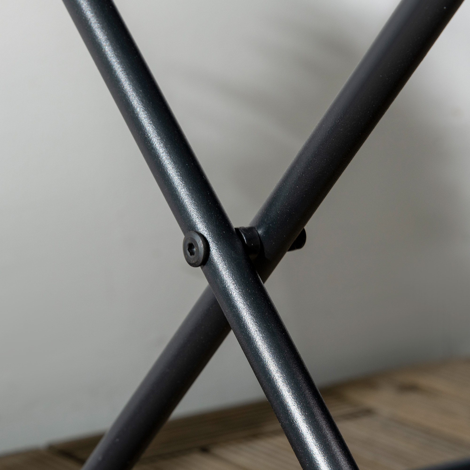Tre tubi metallici neri si incrociano, uno fissato con vite. Pavimento in legno.