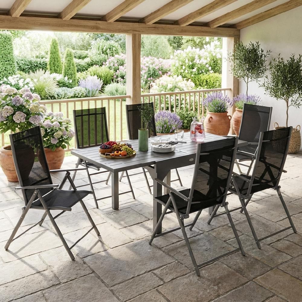 Un set di tavolo e sedie in metallo grigio scuro su un patio pavimentato con vista sul giardino.