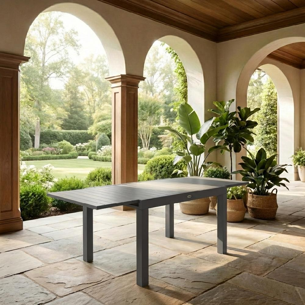 Un tavolo da pranzo grigio si trova su un patio di pietra sotto archi che si affacciano su un giardino.