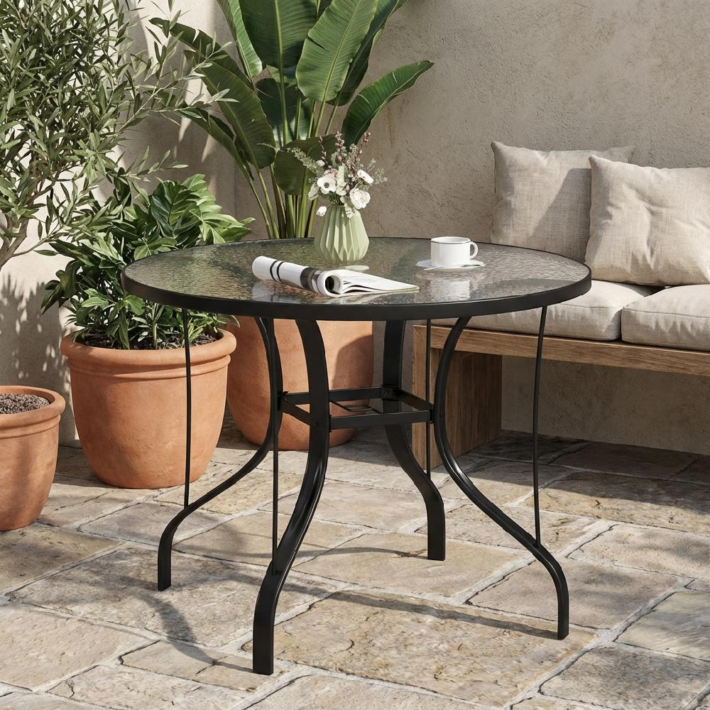 Un tavolo rotondo con piano in vetro e base in metallo nero su un patio in pietra.
