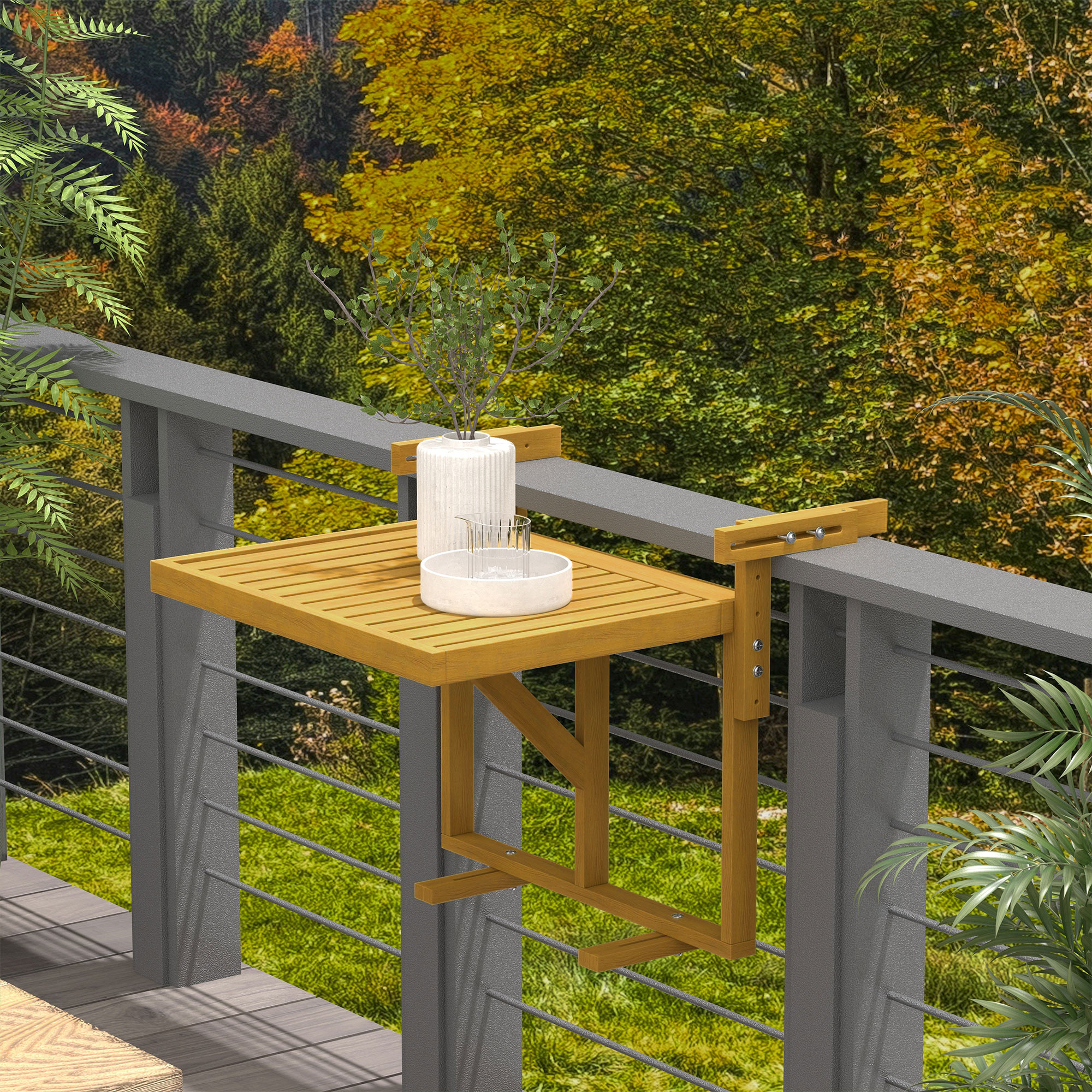 Un tavolo da balcone in legno con una pianta e bicchieri, fissato a una ringhiera grigia, con vista su una foresta autunnale.