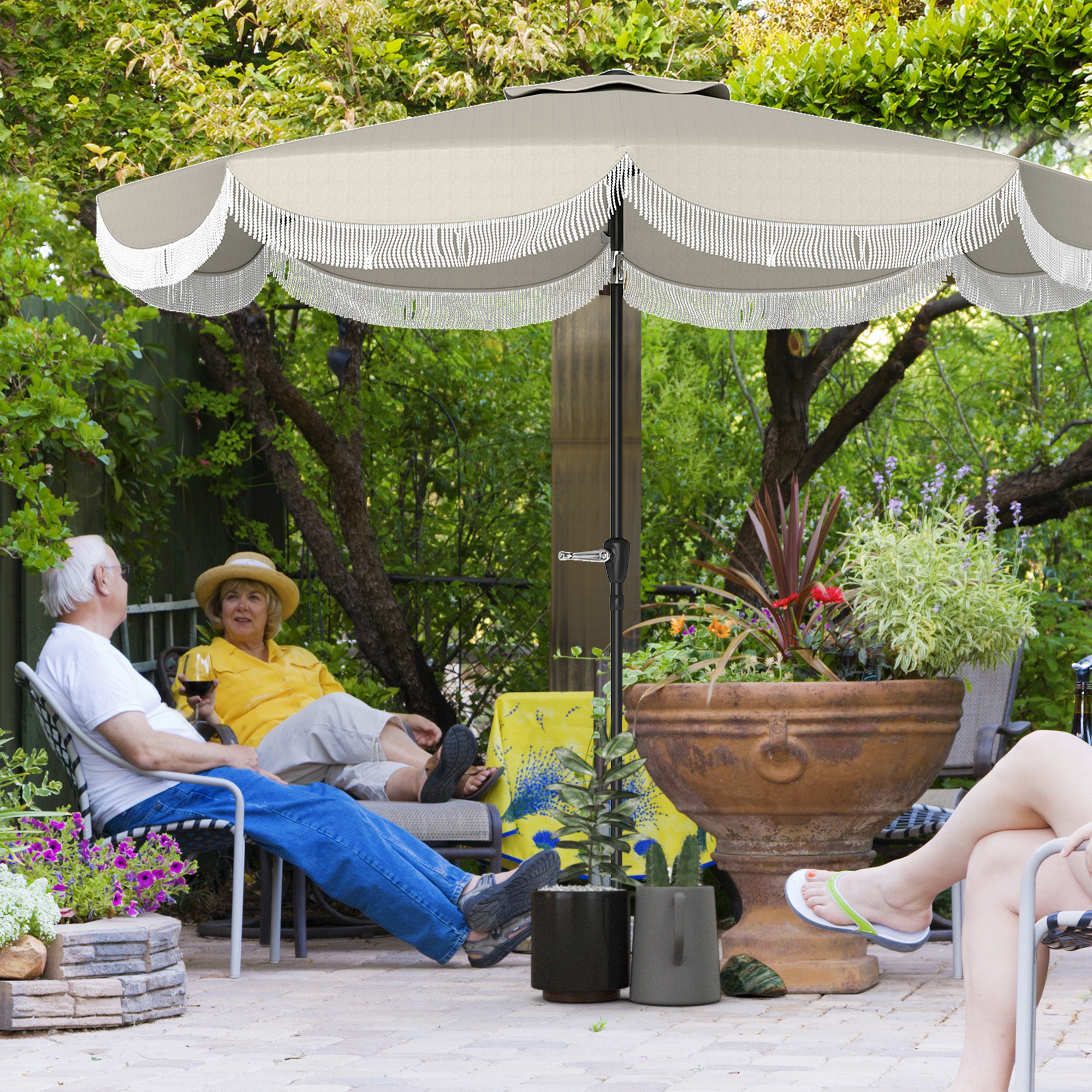 Due coppie si rilassano in giardino sotto un ombrellone. Un uomo tiene un bicchiere di vino.
