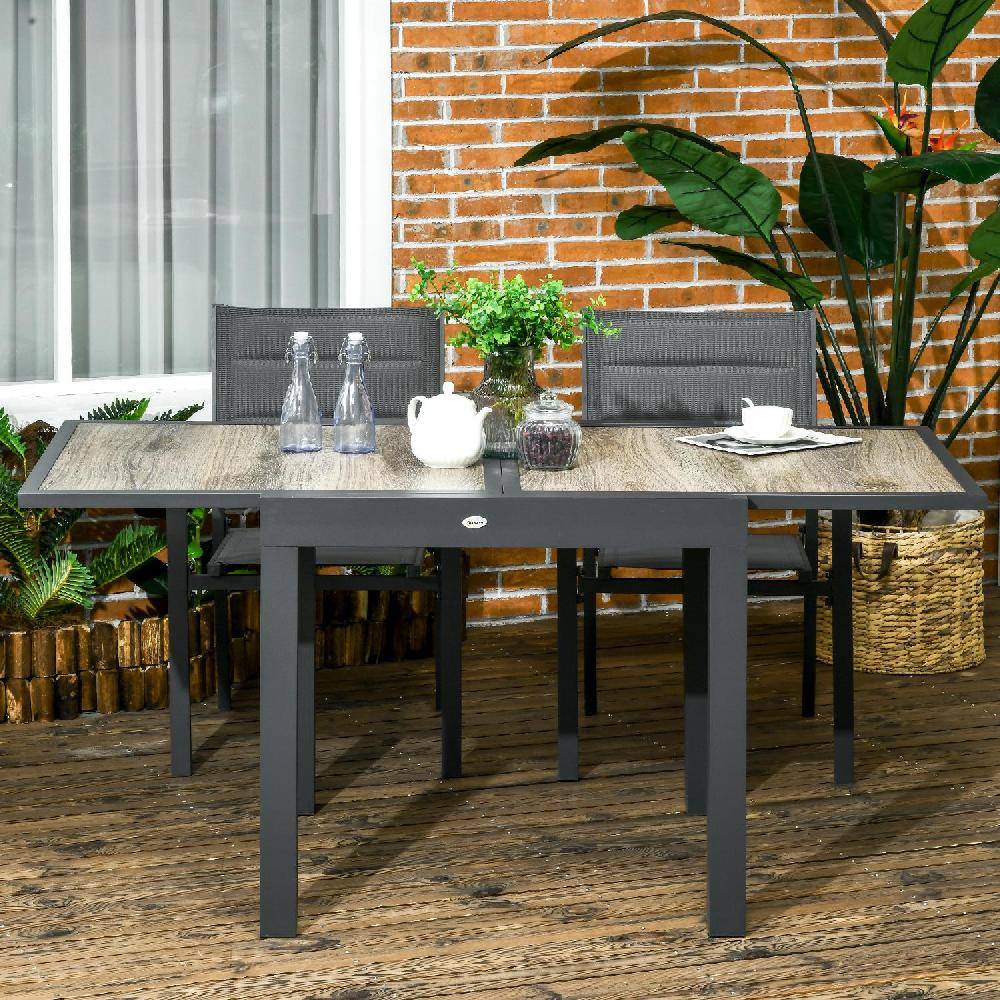 Set da patio moderno con tavolo effetto legno, sedie grigie e piante su terrazzo in legno.