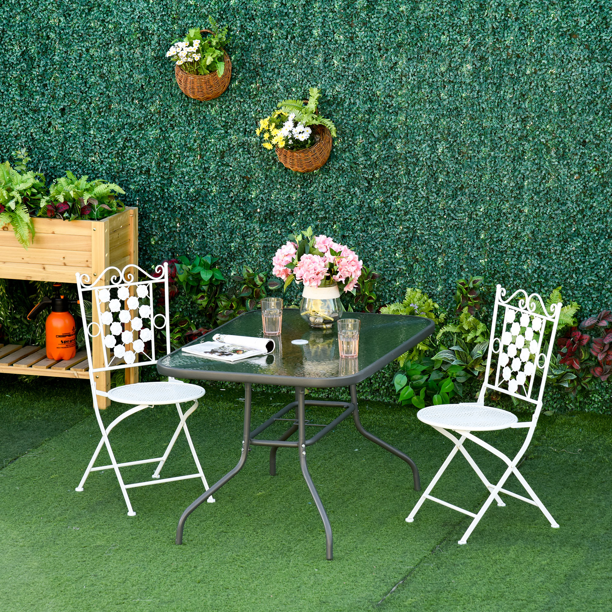 Tavolo da giardino con due sedie bianche davanti a un muro verde con cesti di fiori.