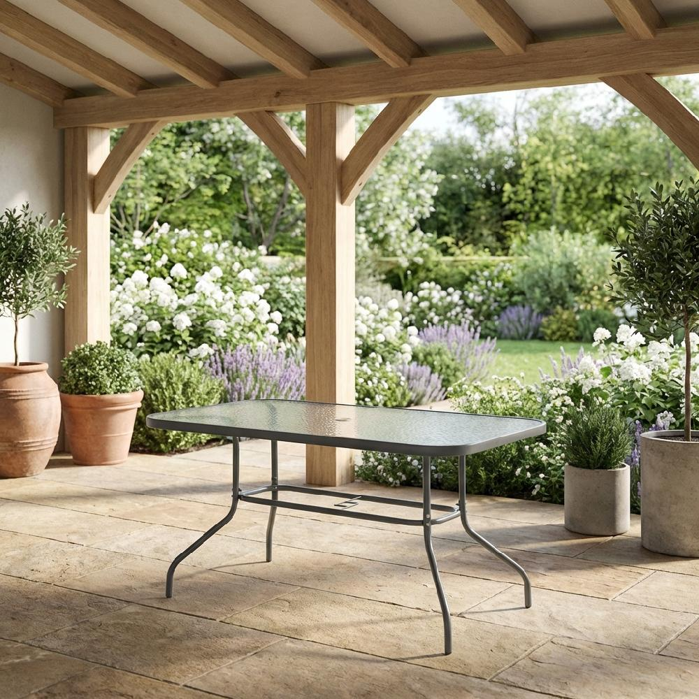Un tavolo con piano in vetro si trova su un patio di pietra con uno sfondo di giardino.