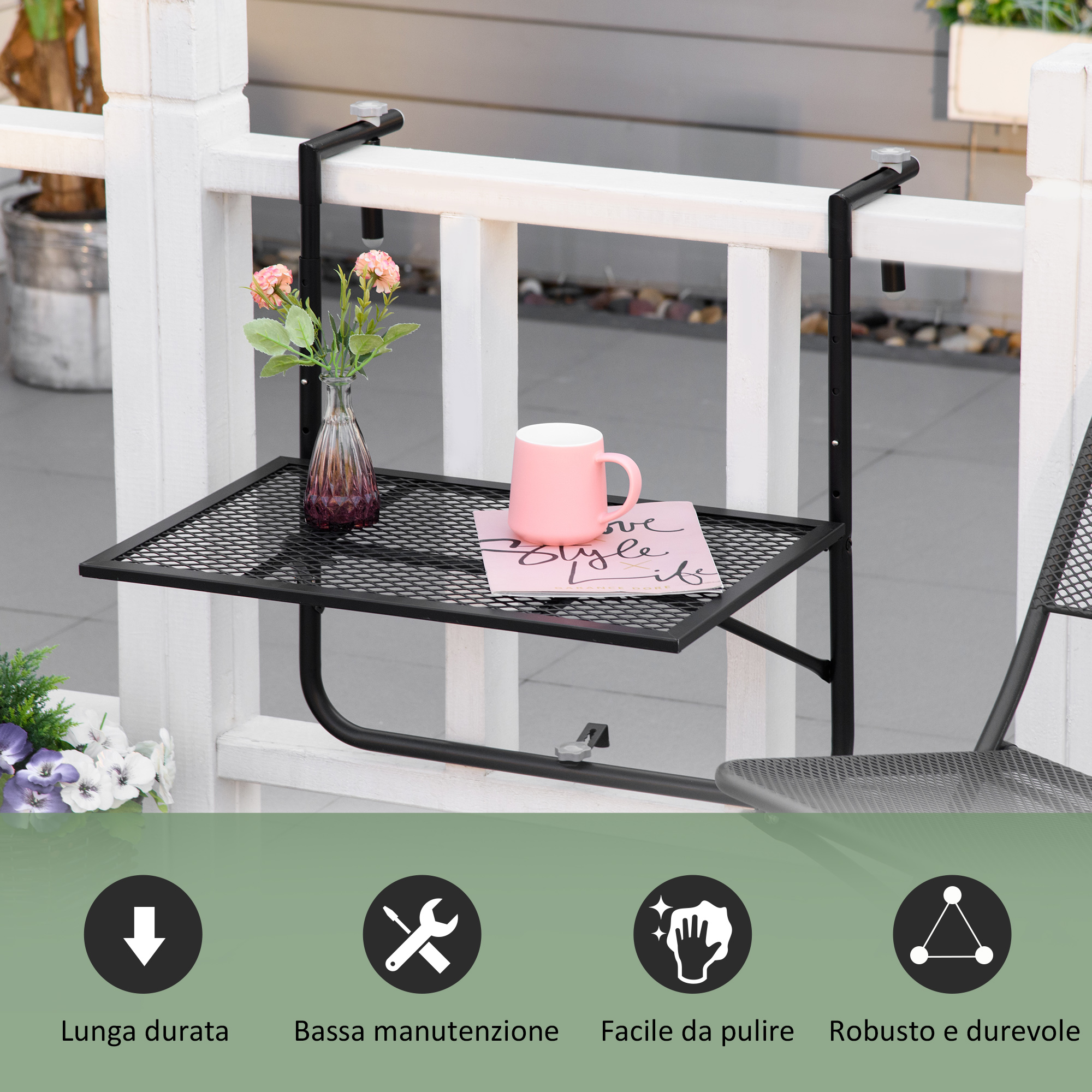 Un tavolino nero da balcone è appeso a una ringhiera bianca. Sopra ci sono un vaso con fiori e una tazza rosa.