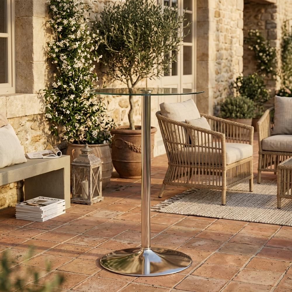 Patio con tavolo in vetro, poltrone in vimini e piante davanti a un edificio in pietra.