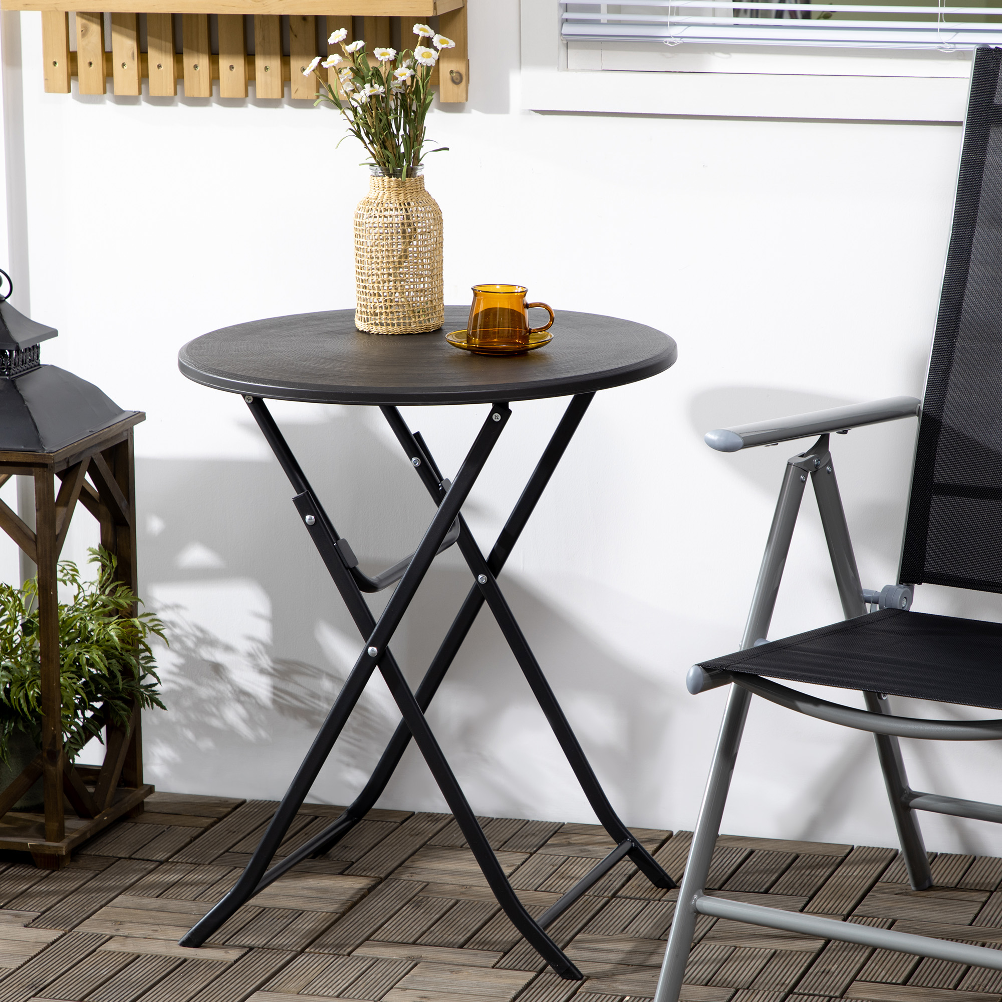 Tavolo rotondo con vaso intrecciato, fiori e tazza. Accanto, una sedia e un porta lanterna.
