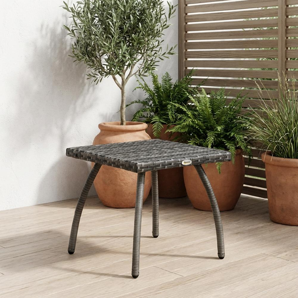 Tavolino grigio in rattan su terrazza in legno con piante e vasi in terracotta.