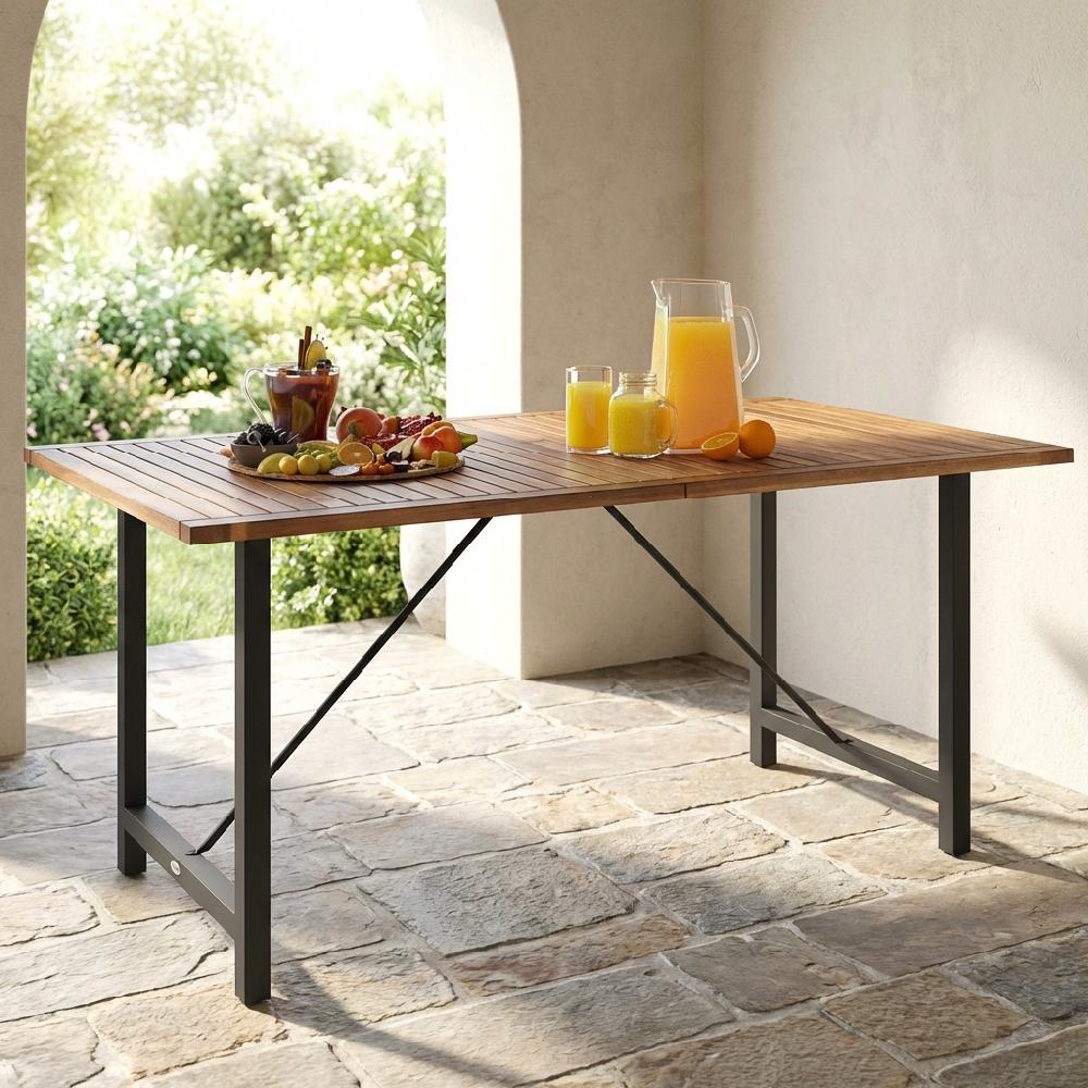 Un tavolo di legno con bevande e frutta è apparecchiato su un patio di pietra con vegetazione.