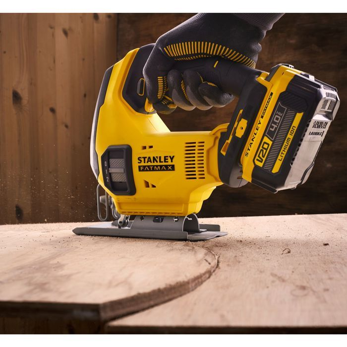 Eine gelbe Stichsäge mit Akku schneidet ein Holzbrett. Staub wirbelt auf.