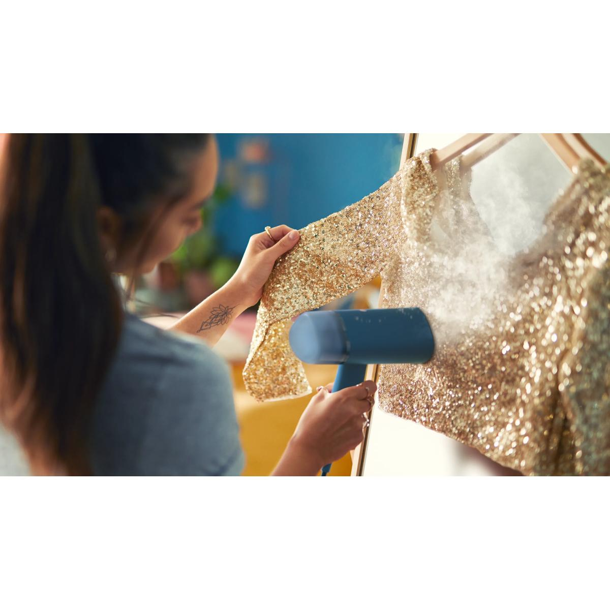 A woman steams a sparkly gold garment with a handheld steamer.