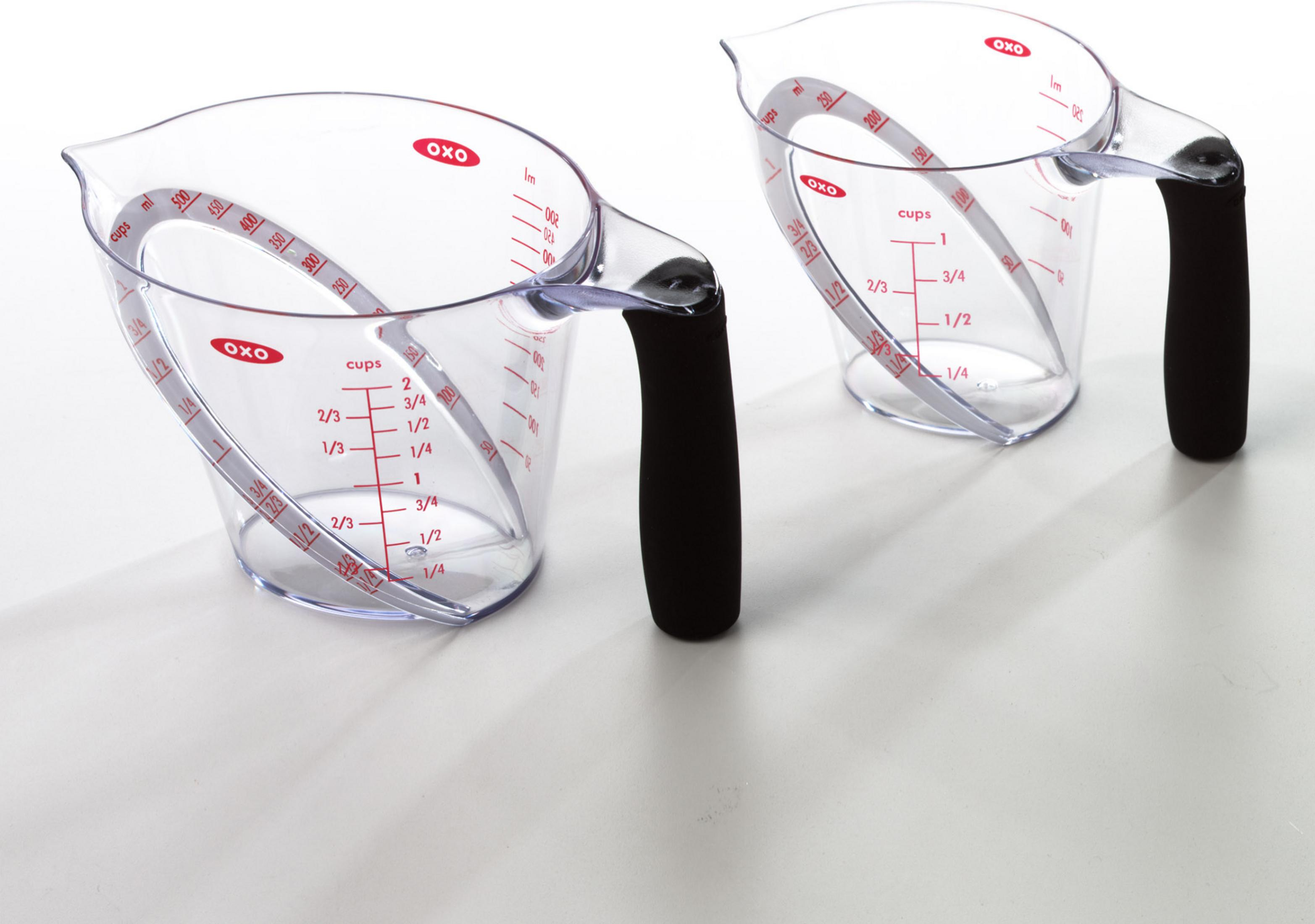 Zwei transparente Messbecher mit schwarzen Griffen stehen auf einer weißen Oberfläche.