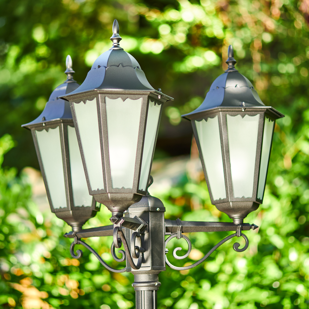 Eine Stehlampe mit drei Lichtern im Freien, umgeben von grünem Laub.