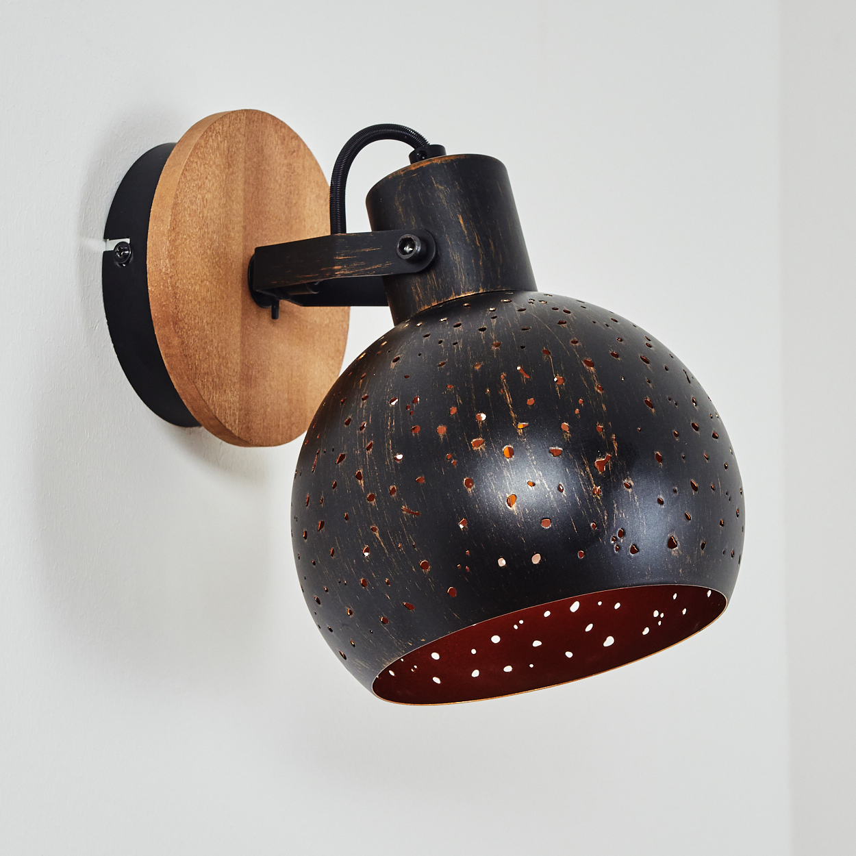 Eine Wandleuchte mit schwarzem Lochmuster-Schirm, Holzsockel und Metallarm.