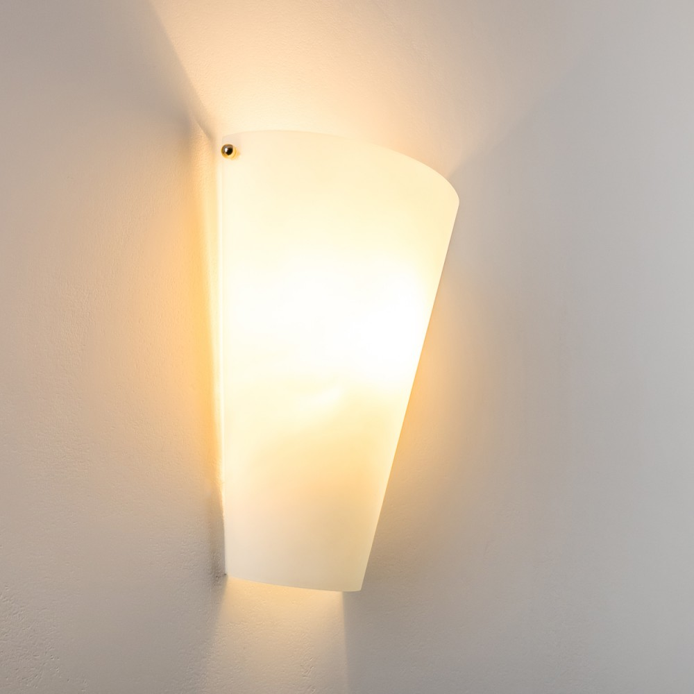 Eine weiße Milchglas-Wandlampe gibt warmes gelbes Licht gegen eine weiße Wand ab.
