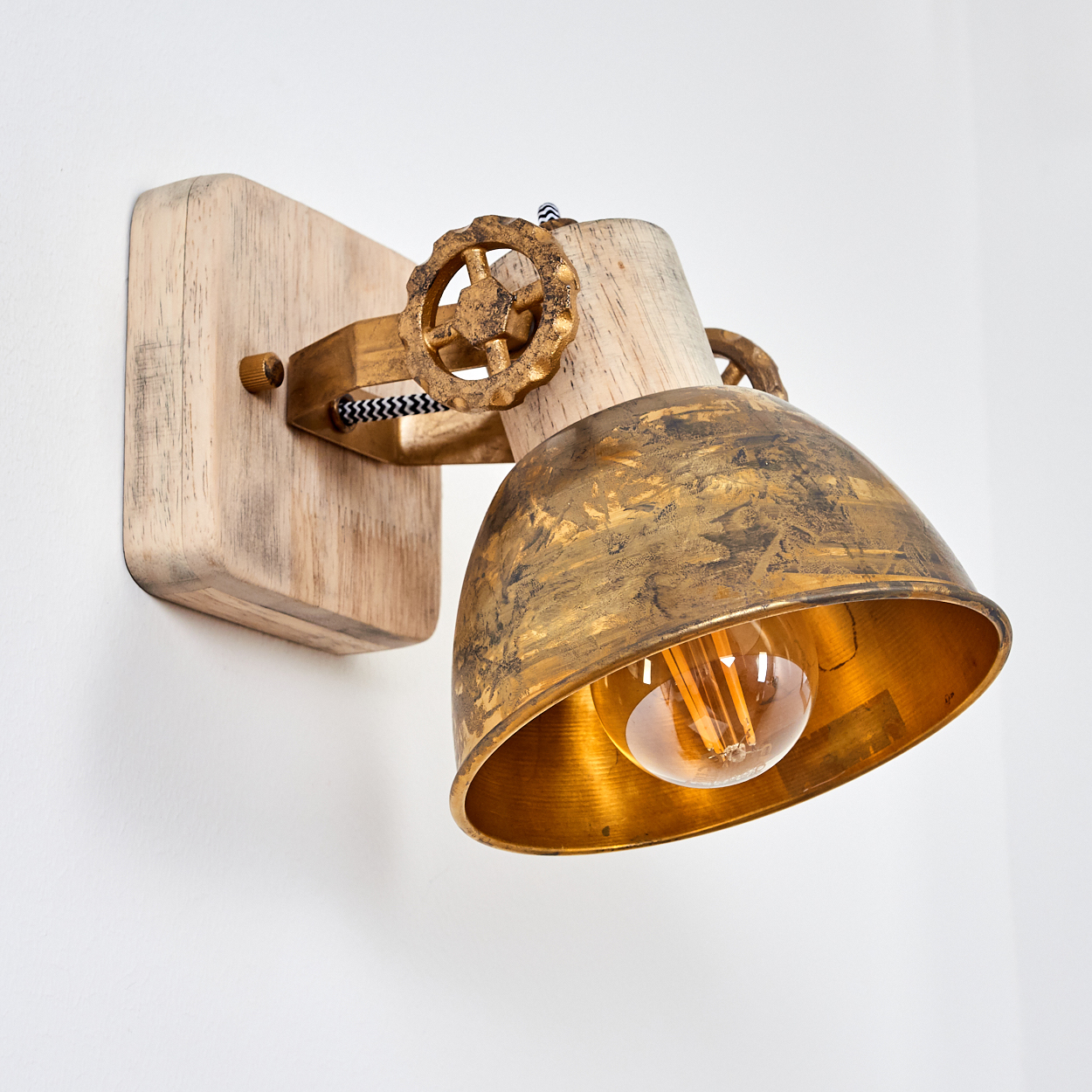 Eine Wandleuchte mit Holzsockel, goldener Metallhaube und sichtbarer Glühbirne.