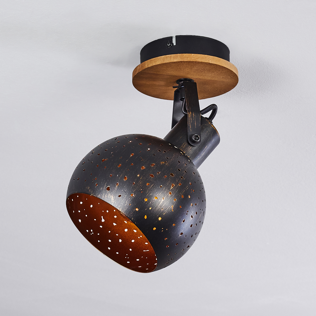 Eine runde, perforierte Lampe mit Holzsockel an einer weißen Decke.