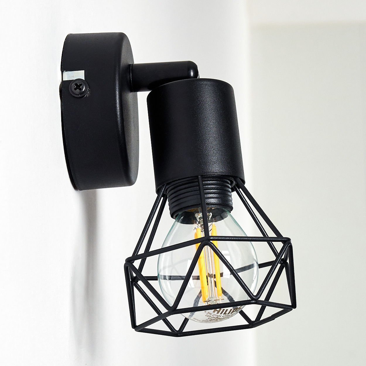 Eine schwarze Käfig-Wandlampe mit klarer Edison-Birne ist an einer weißen Wand montiert.