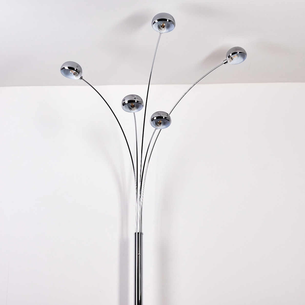 Eine Bogenlampe aus Chrom mit fünf verstellbaren Lichtern vor einer weißen Wand.