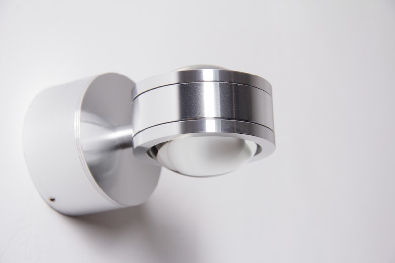 Eine silberne Wandleuchte mit kugelförmigem Diffusor und drehbarem Kopf.