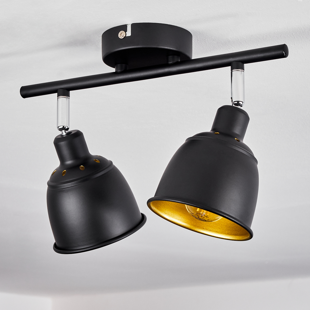 Zwei schwarze Deckenleuchten mit goldenen Innenseiten auf einer Stange.