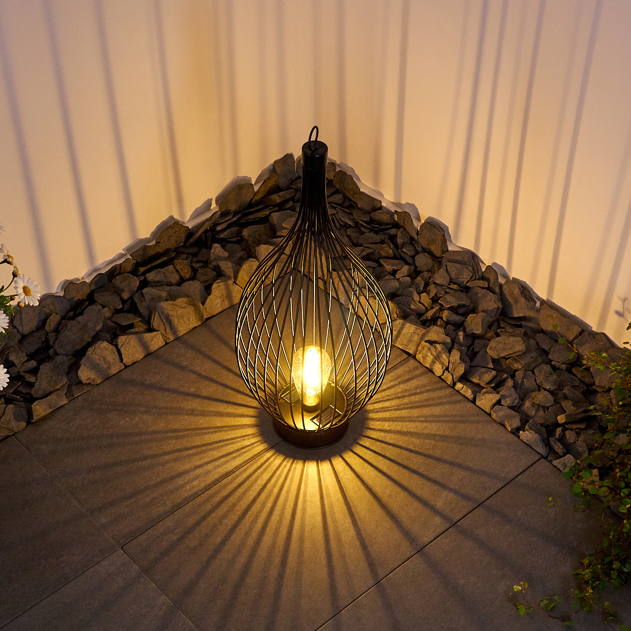 Eine Drahtlampe mit Glühbirne wirft Muster auf den Boden und die Wand.