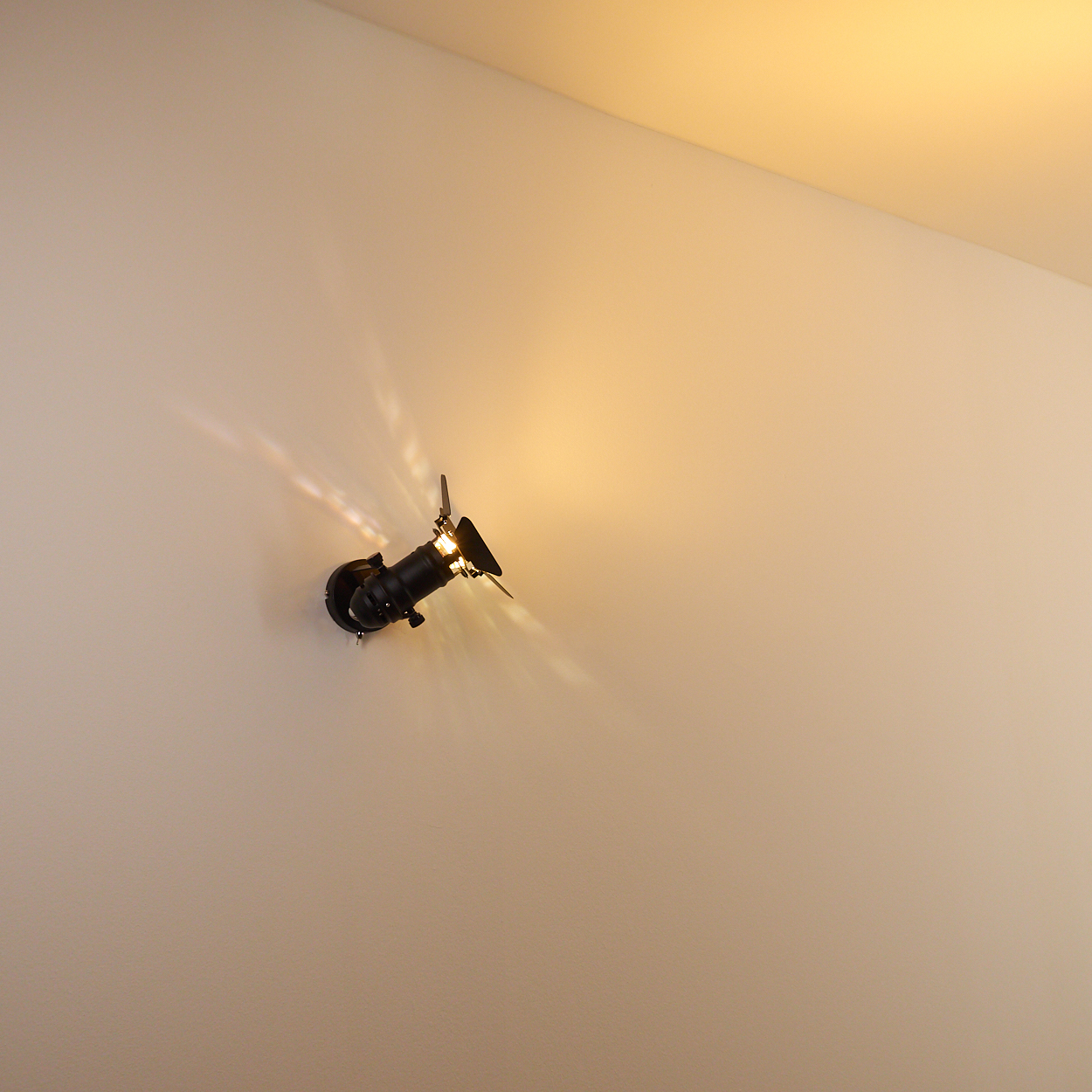 Ein schwarzer Wandstrahler wirft Licht und Schatten auf eine cremefarbene Wand.