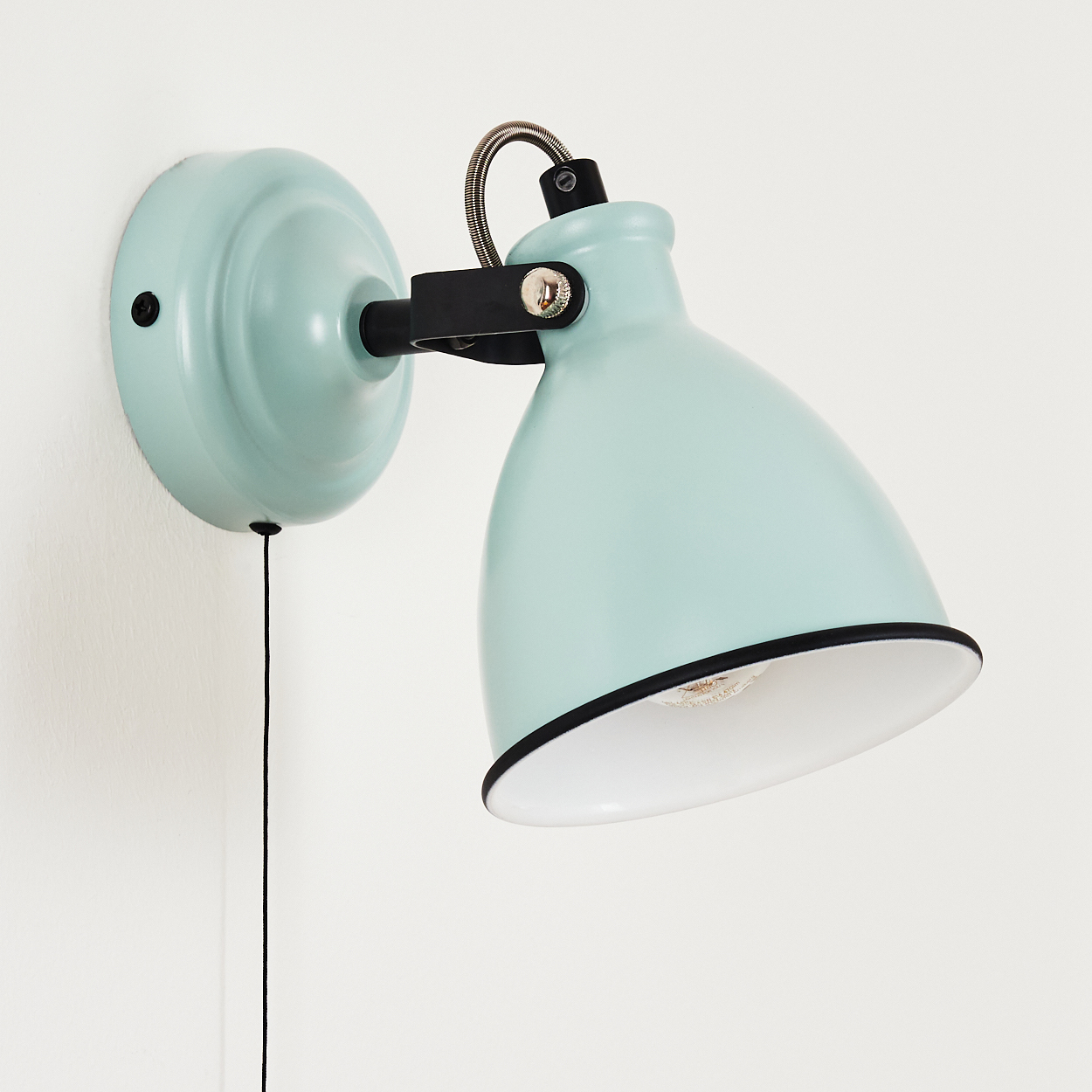Ein türkisfarbener Wandleuchter mit schwarzem Kabel hängt an einer weißen Wand.