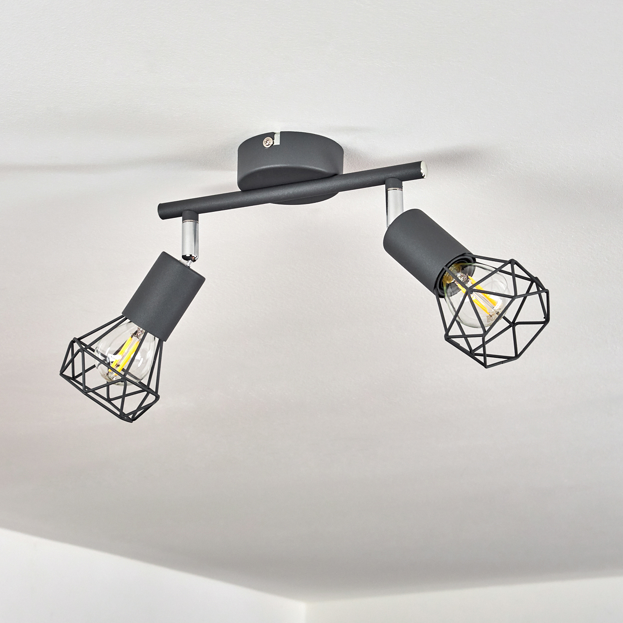 Ein moderner schwarzer Deckenstrahler mit zwei verstellbaren Lampen und geometrischen Käfigen.