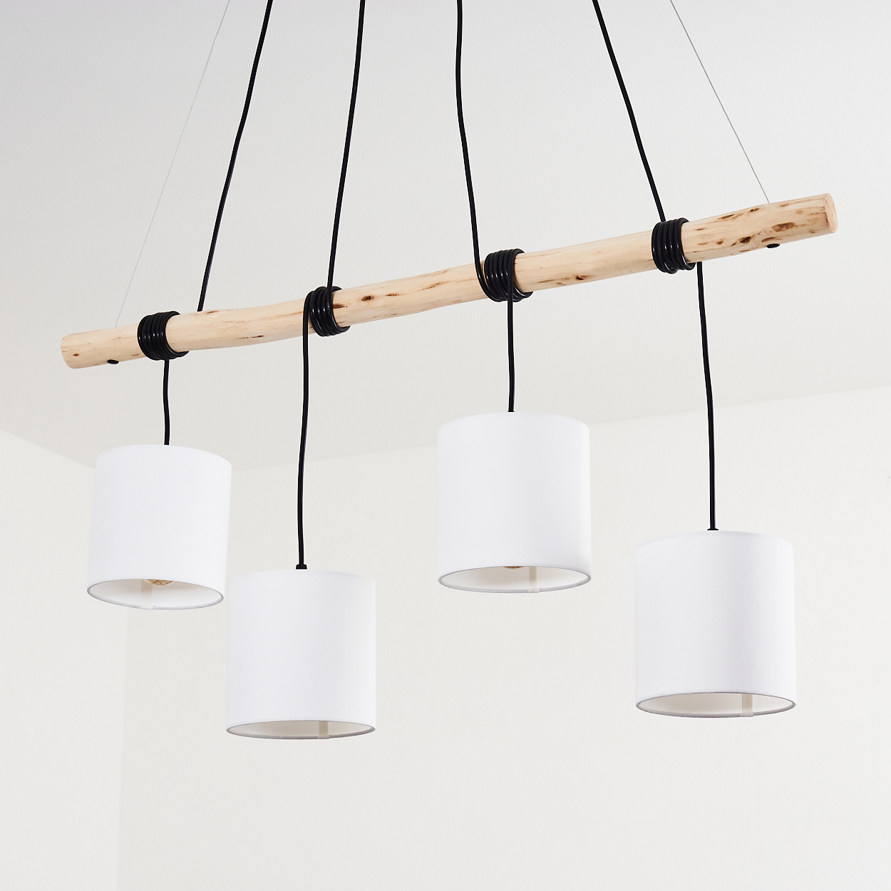 Eine Holzstange mit vier weißen Lampenschirmen, die von schwarzen Kabeln gehalten werden.