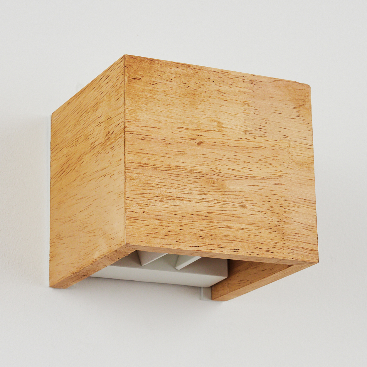Ein kubischer Holzwürfel als Wandleuchte an einer weißen Wand.