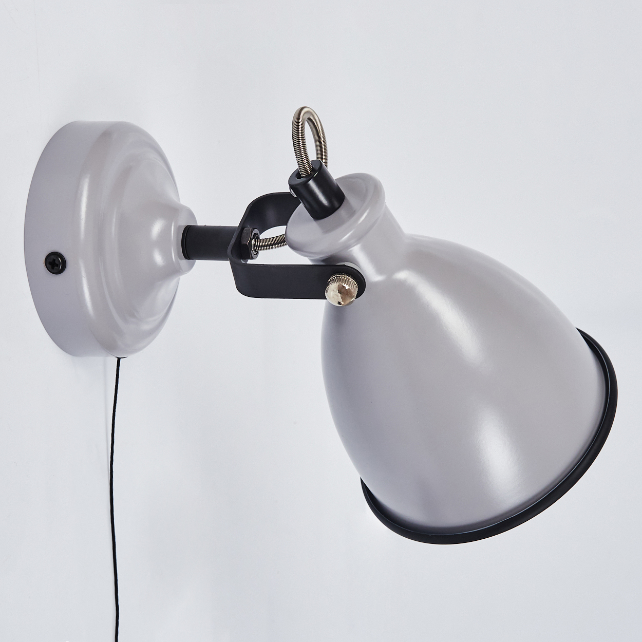 Graue Wandleuchte mit schwarzem Arm und Schirm, an einer weißen Wand montiert.